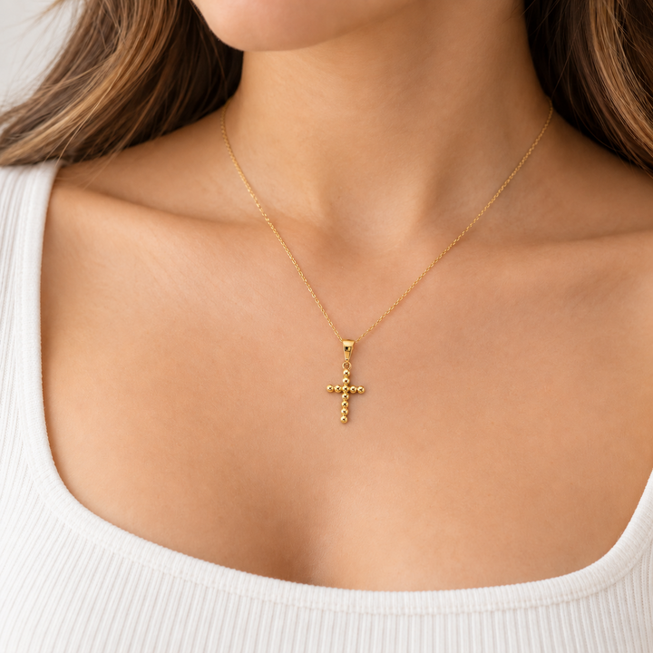 14K yellow gold bead cross pendant worn on a necklace